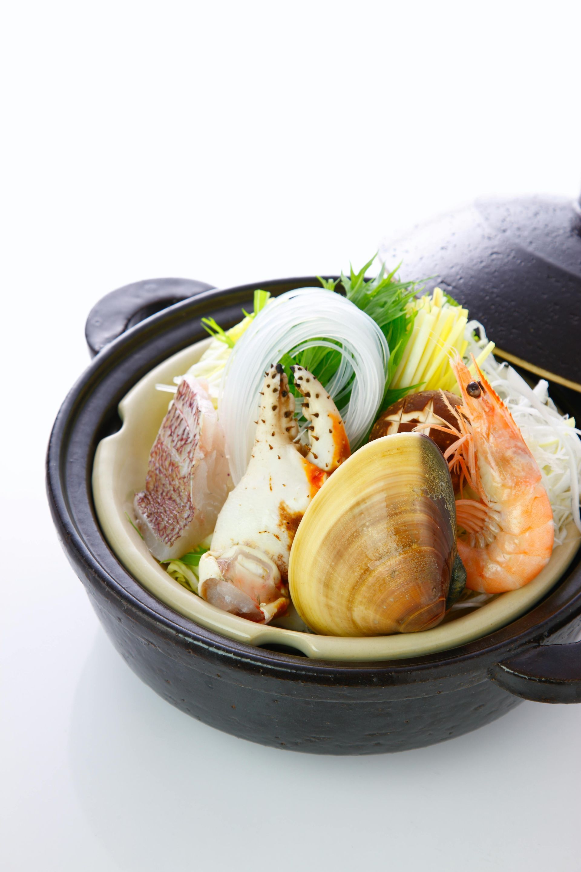 A pot filled with seafood and noodles on a white surface.