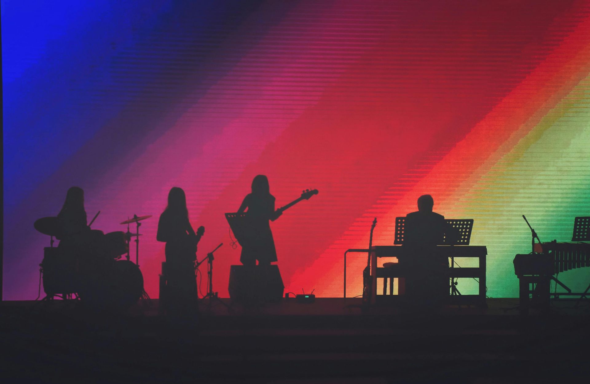 A group of people playing instruments on a stage with a rainbow in the background.