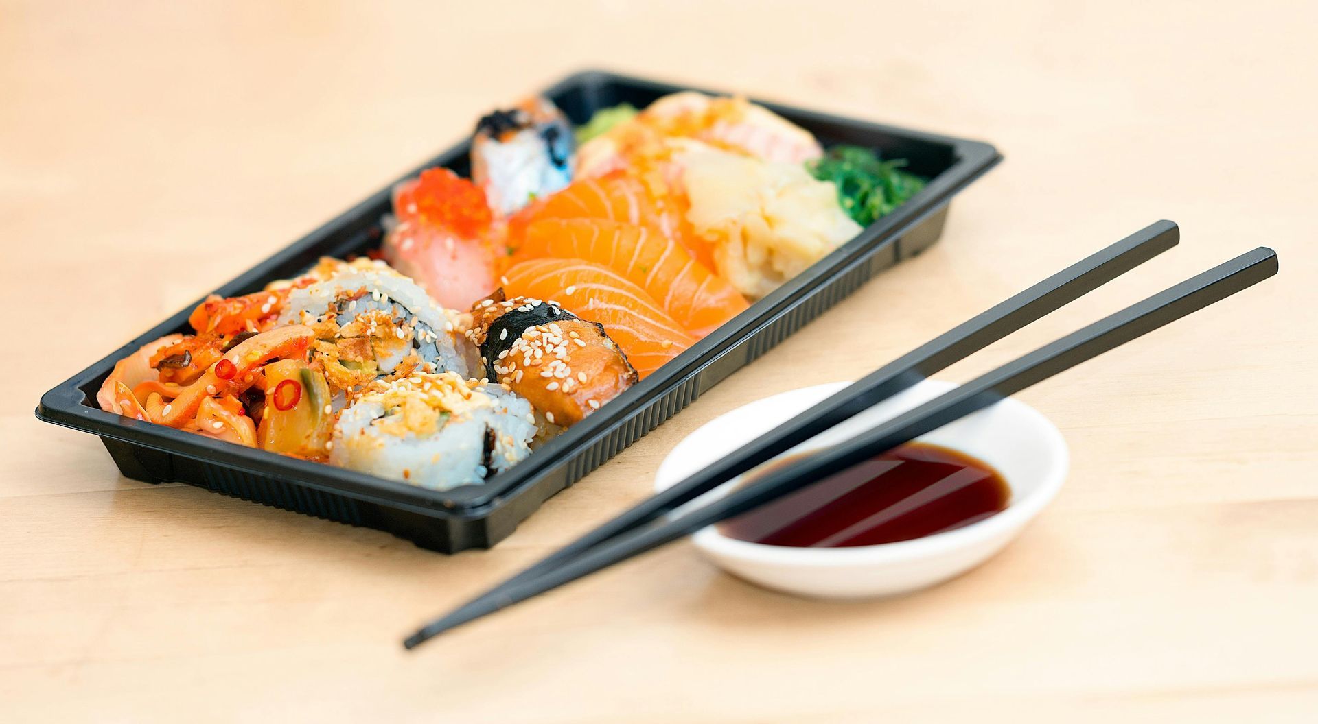 A tray of sushi with chopsticks and soy sauce on a wooden table.
