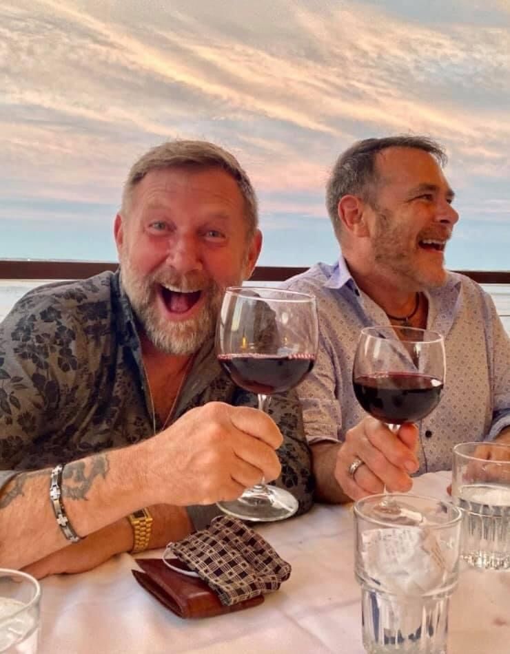 Two men are sitting at a table drinking wine and laughing.