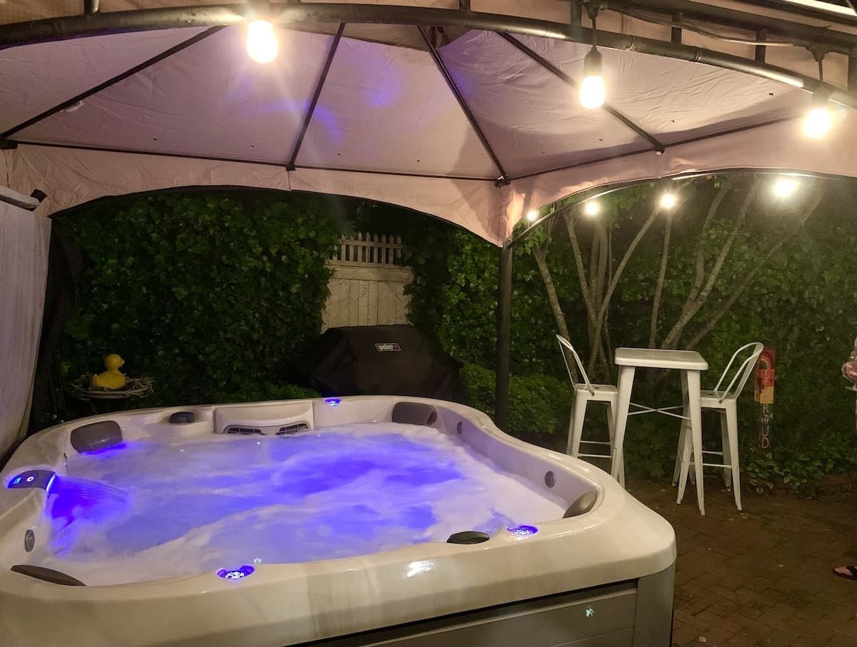 A hot tub is sitting under a tent in a backyard.
