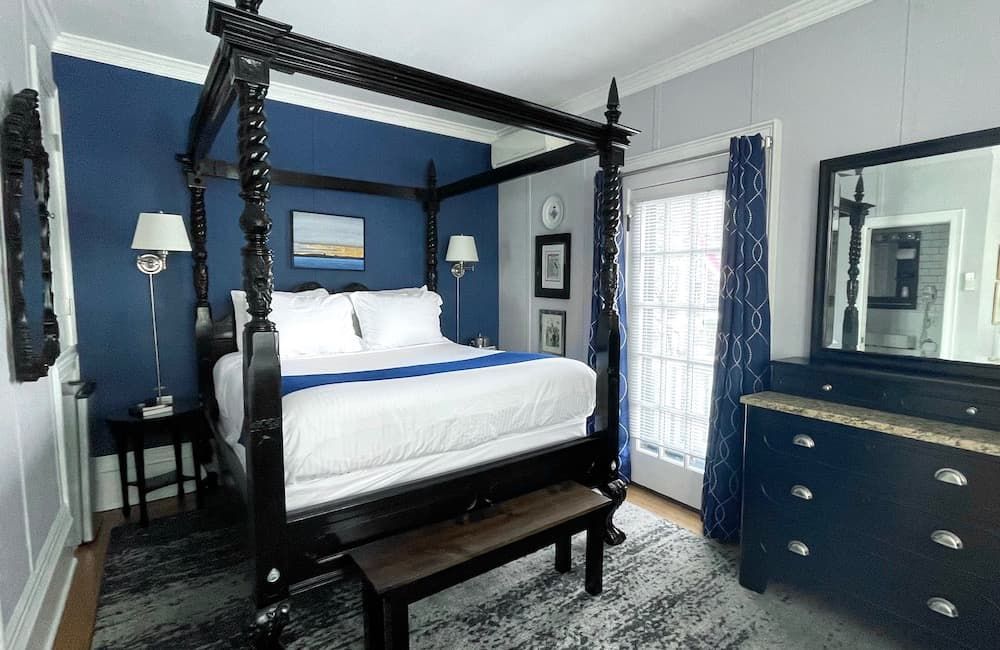 A bedroom with a canopy bed , dresser , mirror and bench.