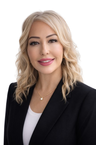 A person with shoulder-length blonde hair wearing a black blazer over a white shirt, posing against a white background.