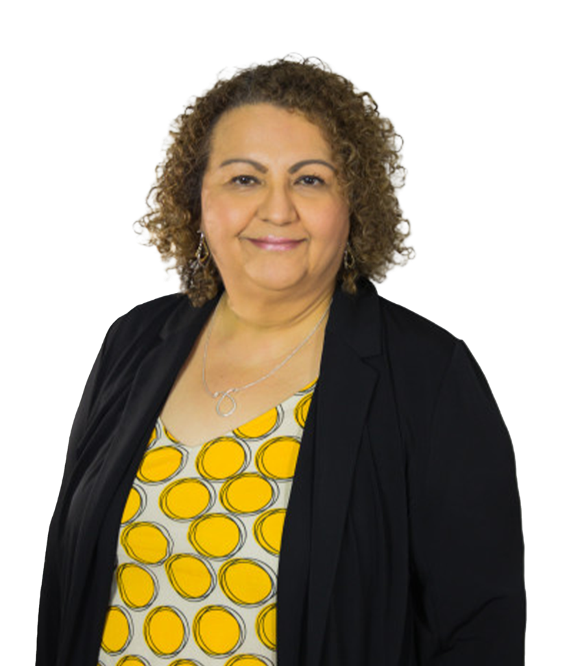 A smiling person with curly brown hair wearing a yellow patterned top and a black blazer against a plain white background.