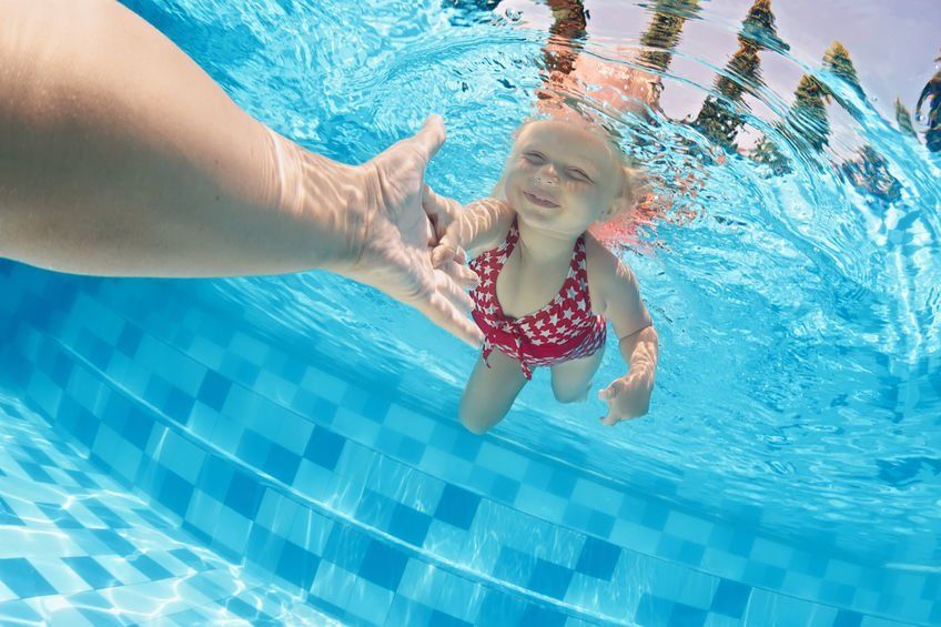 Little girl swimming in a pool holding an adults hand