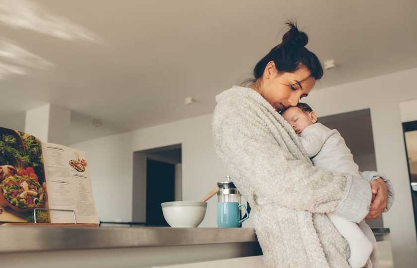 Mom leaning on counter while her baby sleeps on her chest