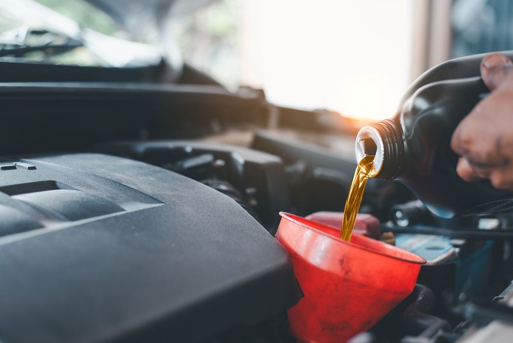 A person is pouring oil into a car through a funnel.