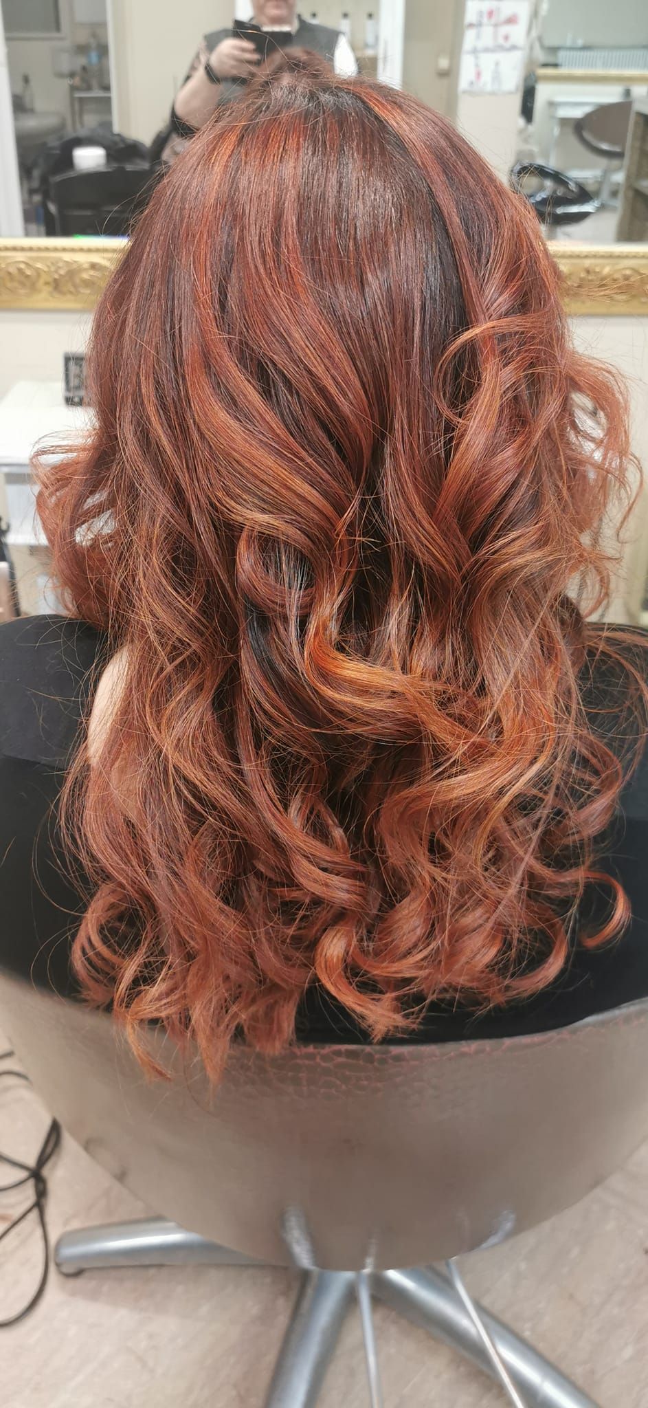 Una donna con i capelli rossi è seduta su una sedia davanti a uno specchio.