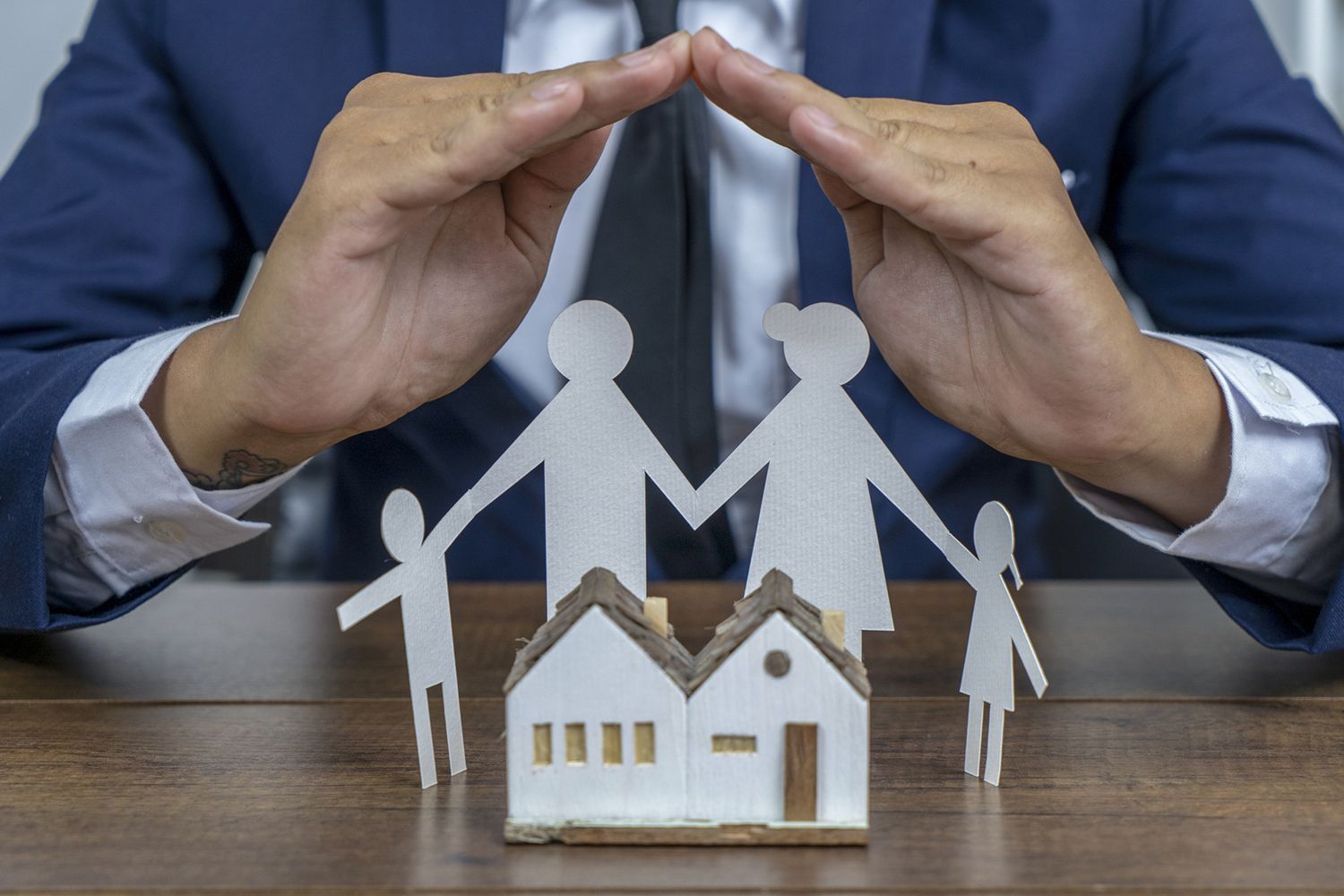 Man's hands sheltering paper family and house models, symbolizing protection, insurance, and security.