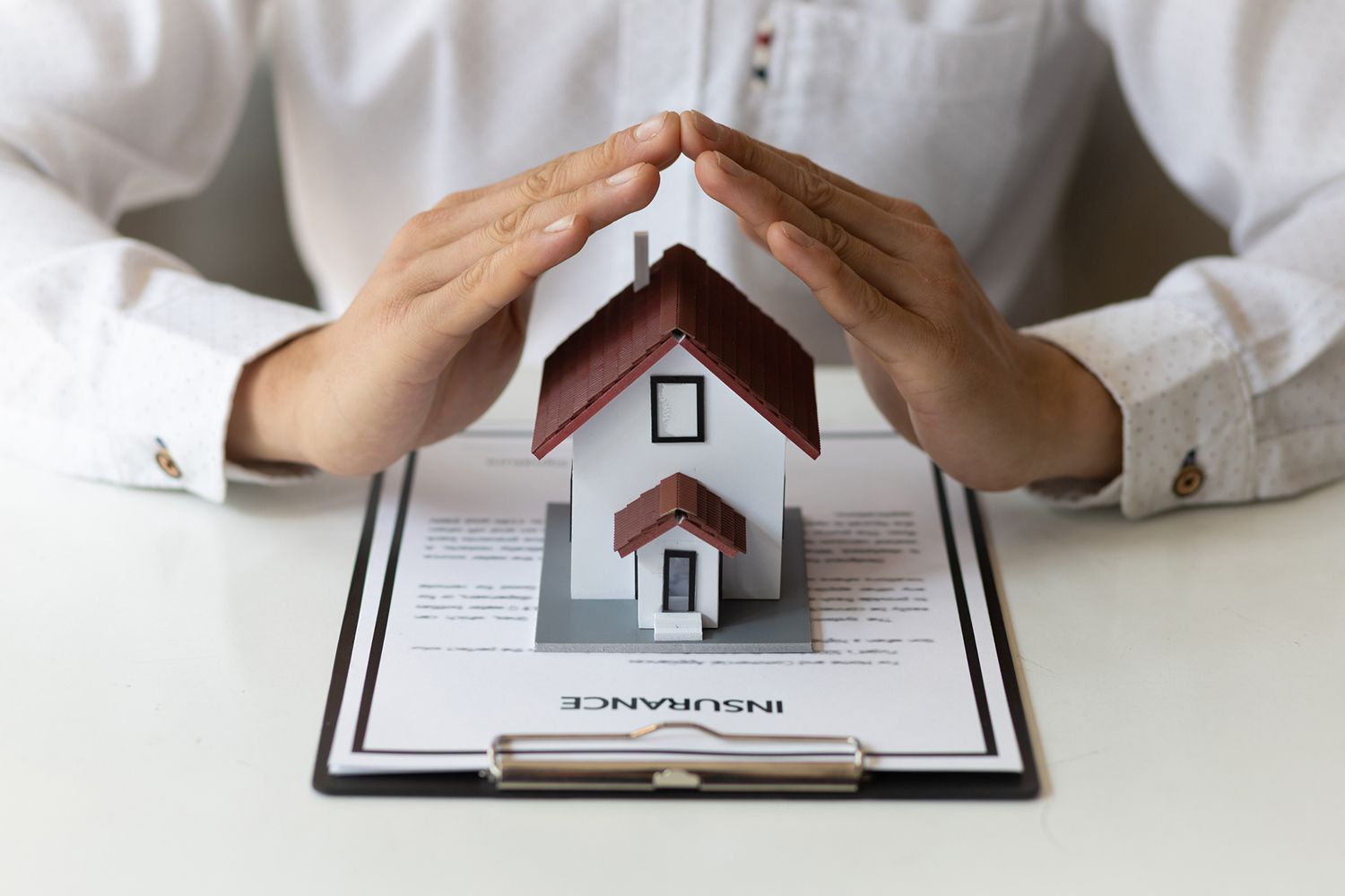 Hands sheltering a model house on top of an insurance document.