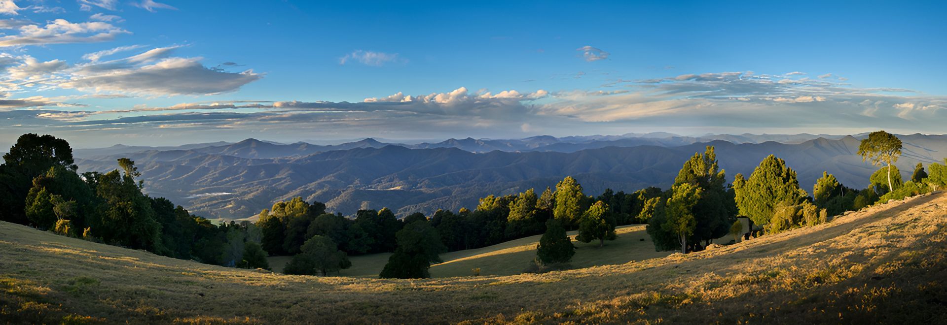 Panoramic view of a hilly landscape under a blue sky, with trees and a grassy field in the foreground — Stuart Pearce Electrical In Coffs Harbour, NSW