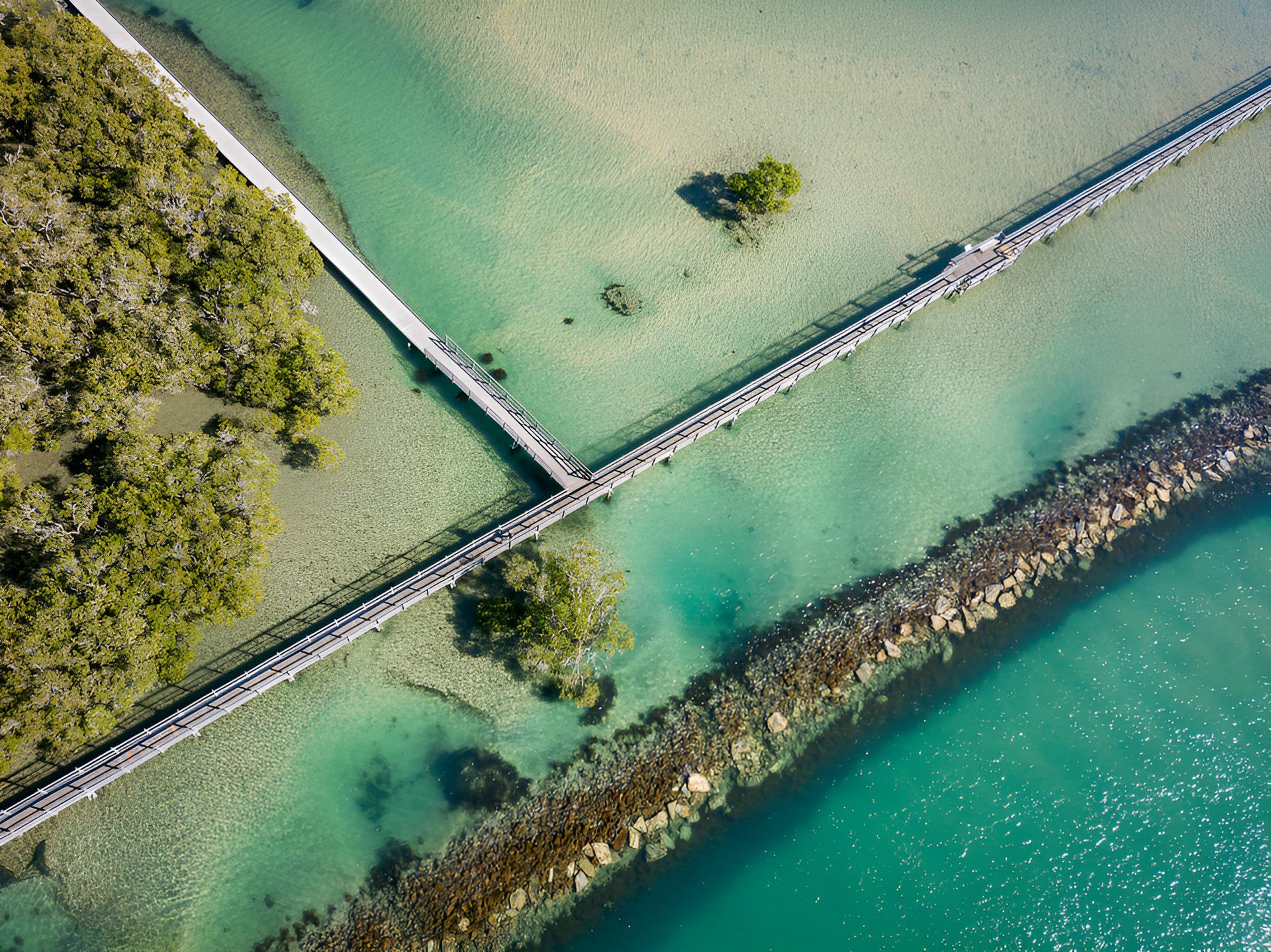 Aerial view of turquoise water with a stone jetty, a boardwalk, and mangrove trees — Stuart Pearce Electrical In Coffs Harbour, NSW