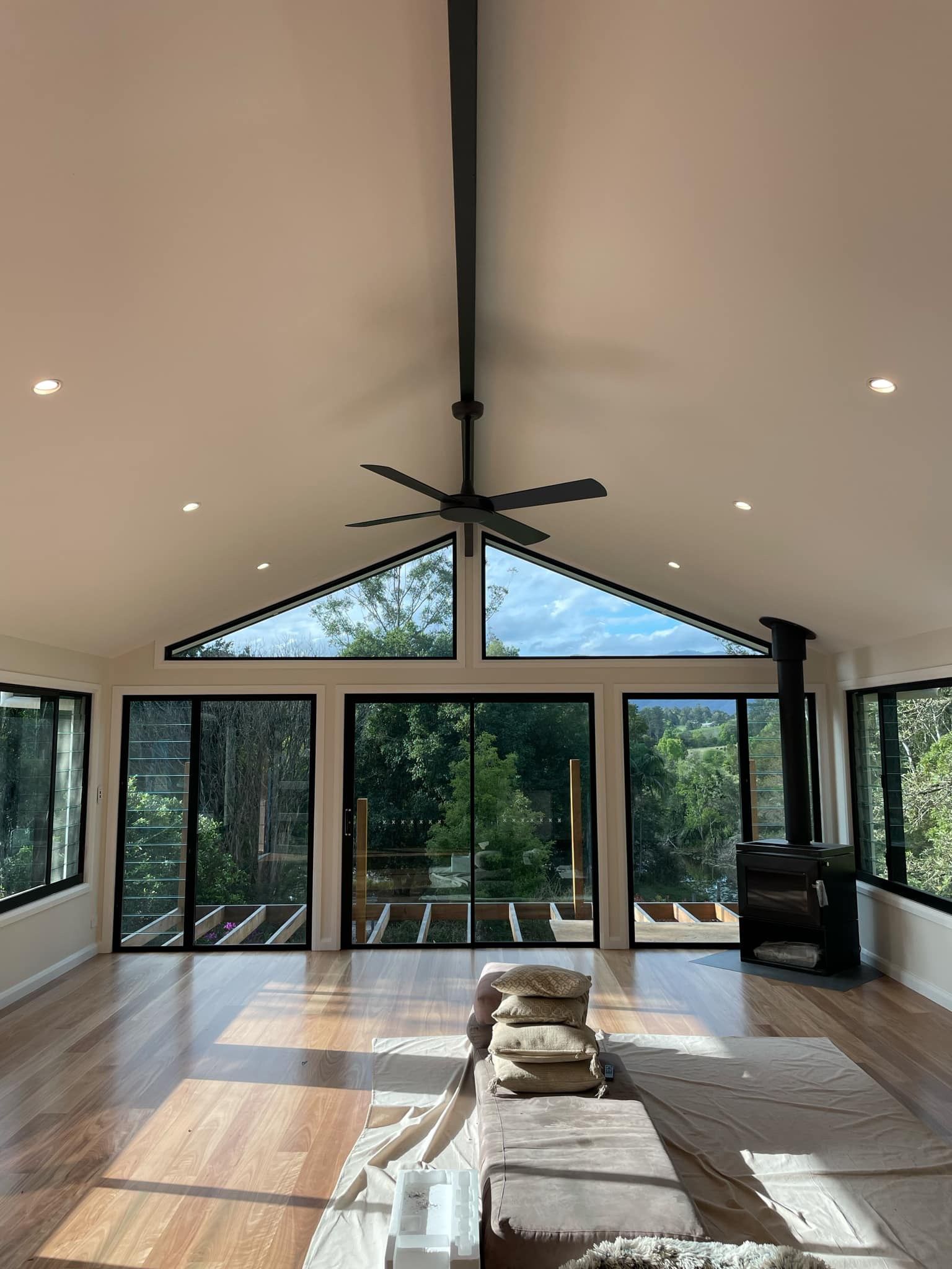 Bright open room with large windows, wooden floor, high ceiling, and a fireplace — Stuart Pearce Electrical In Coffs Harbour, NSW