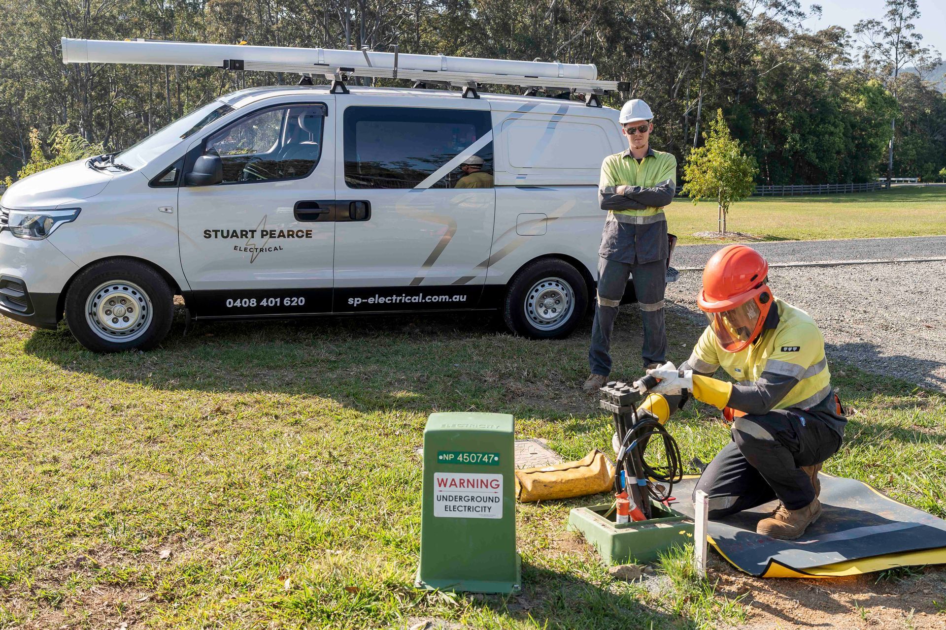Two utility workers near a white van. One kneels, working on a cable — Stuart Pearce Electrical In Coffs Harbour, NSW