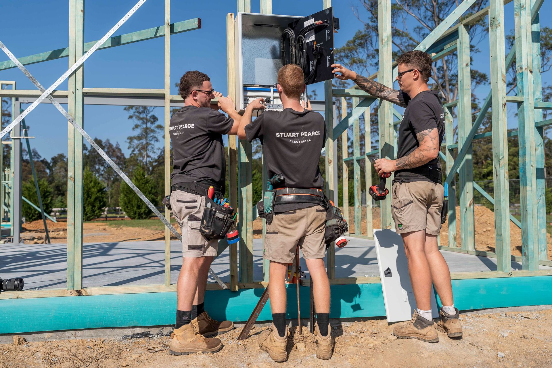 Three electricians installing electrical panel in new home construction — Stuart Pearce Electrical In Coffs Harbour, NSW