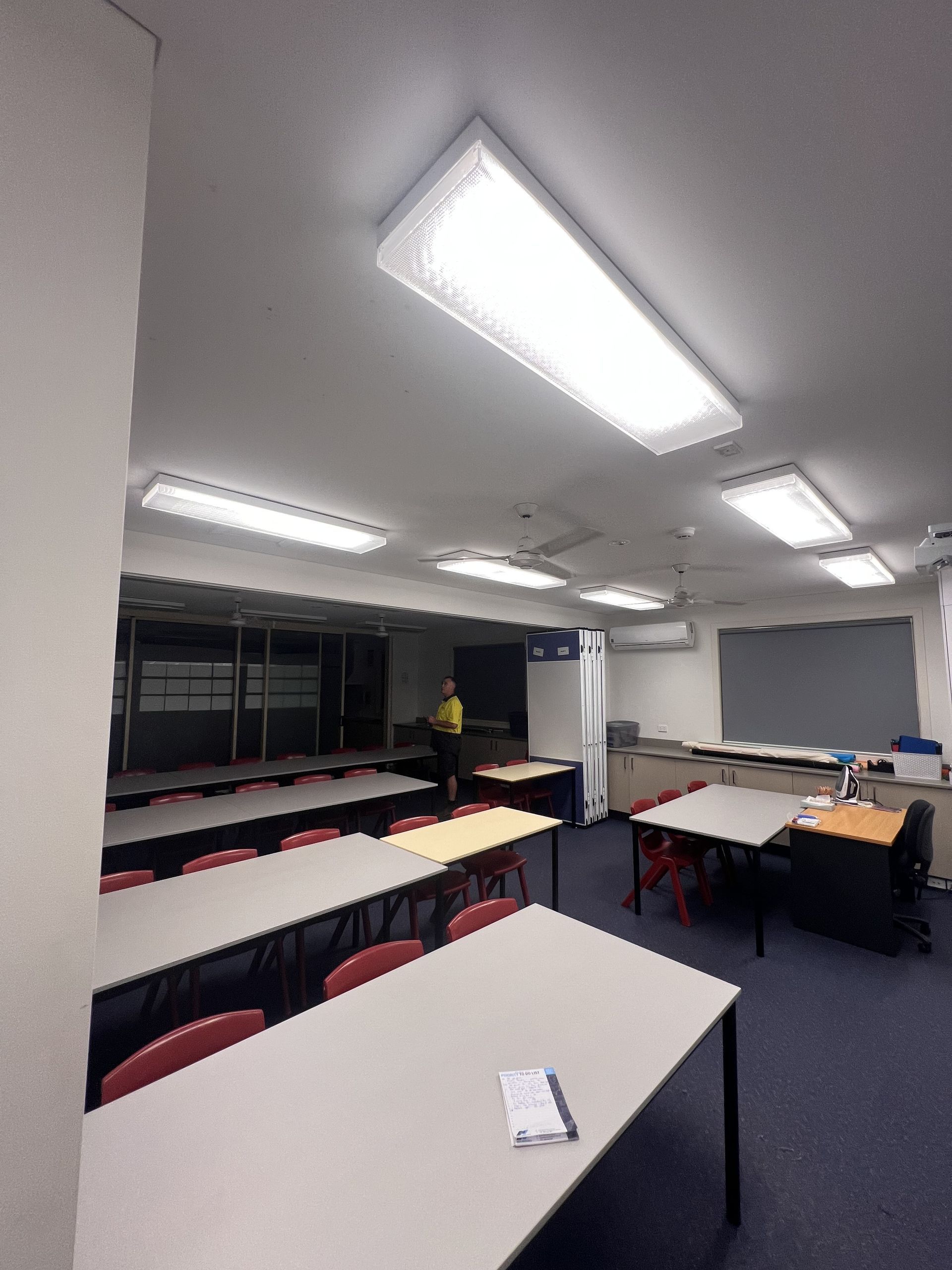 Classroom with rows of desks, a person standing, and fluorescent lights — Stuart Pearce Electrical In Coffs Harbour, NSW