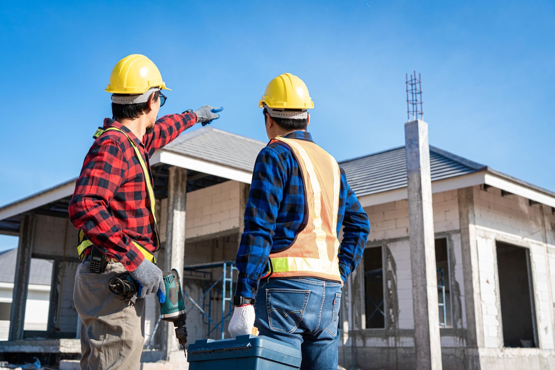 two construction workers are standing in front of a house under construction .