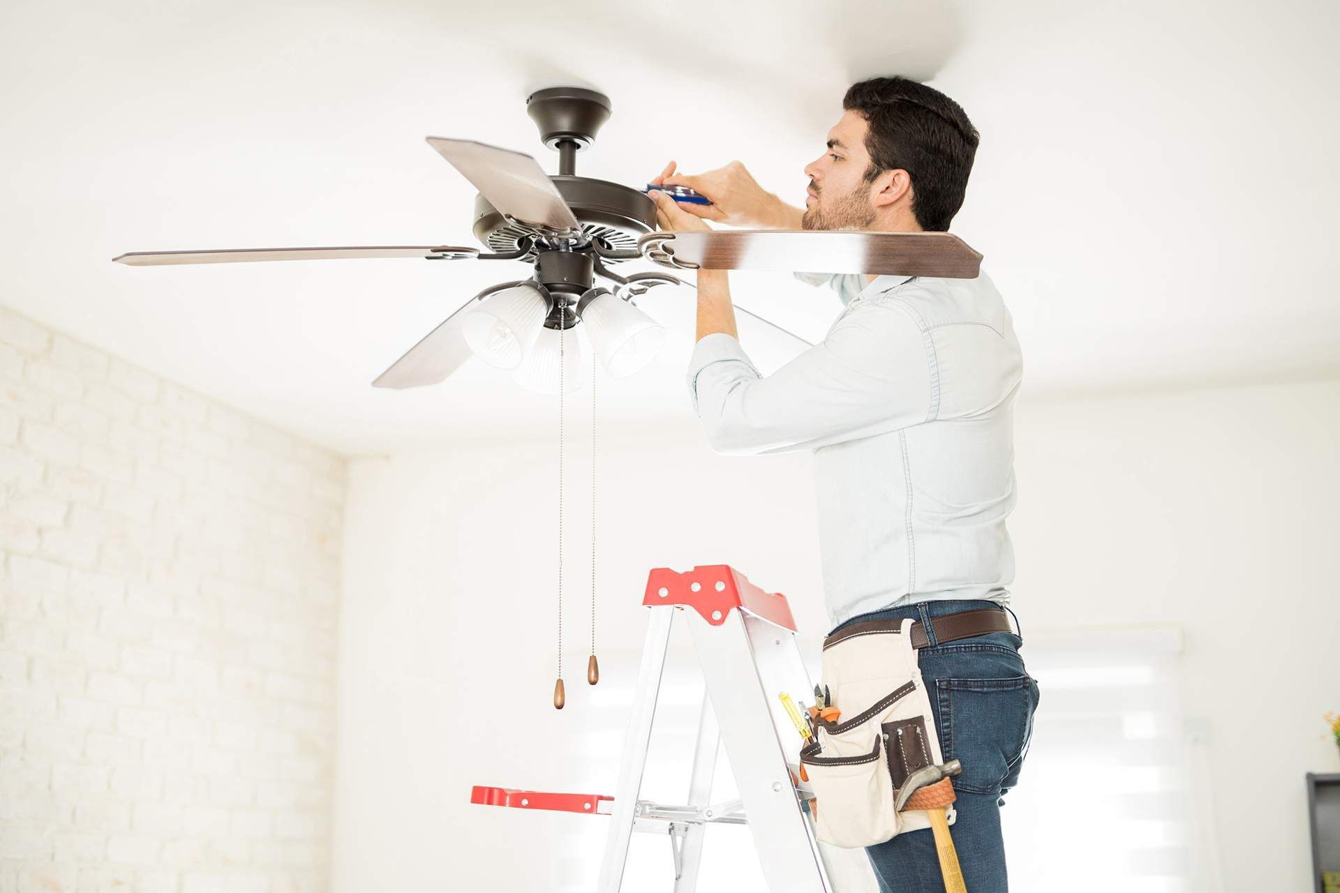 a man is standing on a ladder fixing a ceiling fan .