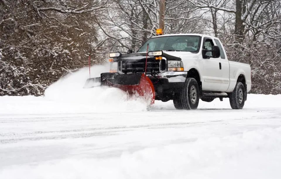 White snowplow truck clearing snow from a road on a snowy day.
