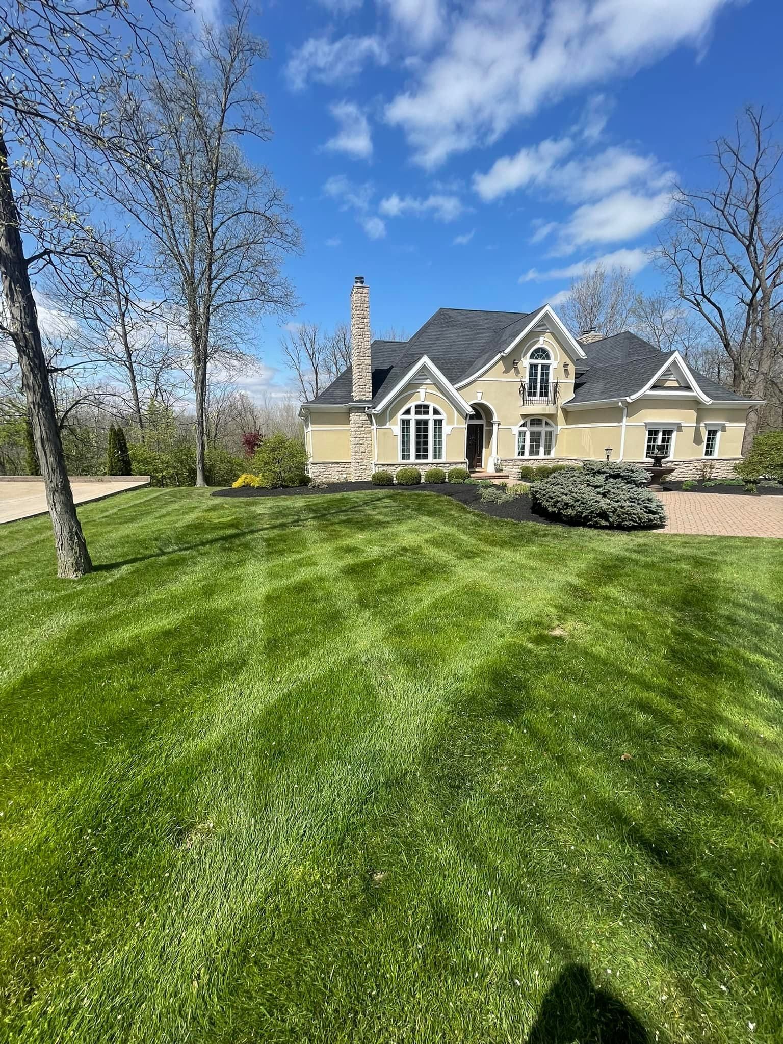 Luxurious beige house on a green lawn under a blue sky with fluffy clouds.