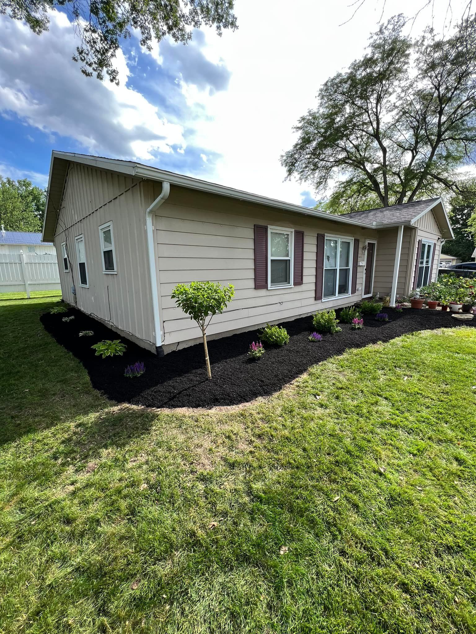 Tan house with black mulch landscaping, green lawn, and blue sky.