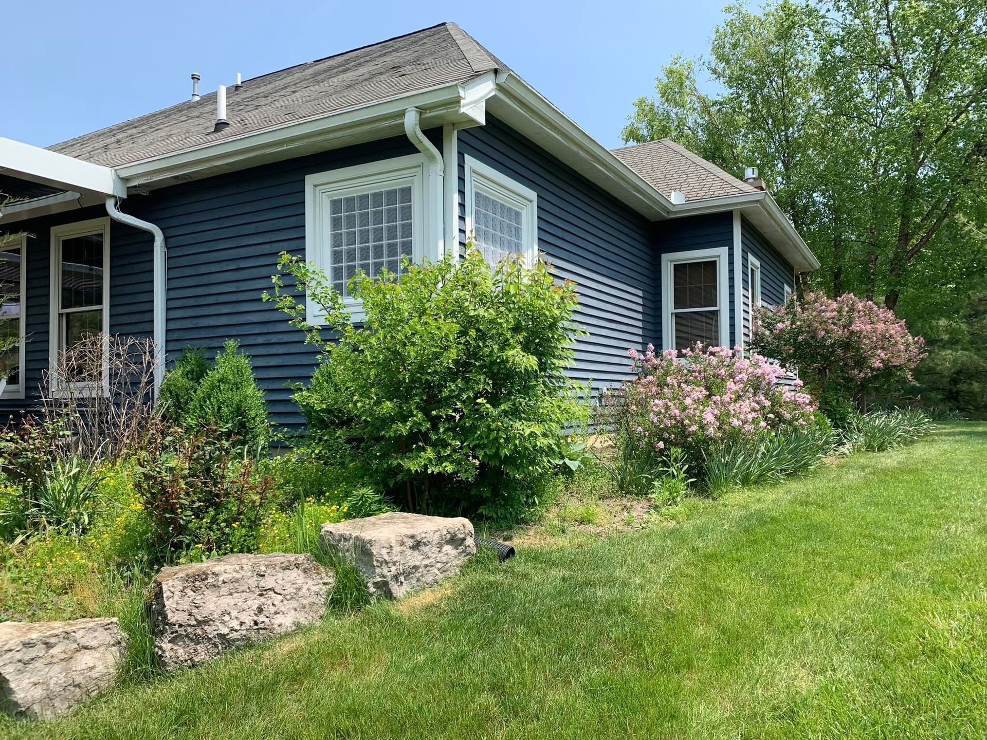 Blue house with white trim and garden, grassy yard, sunny day.