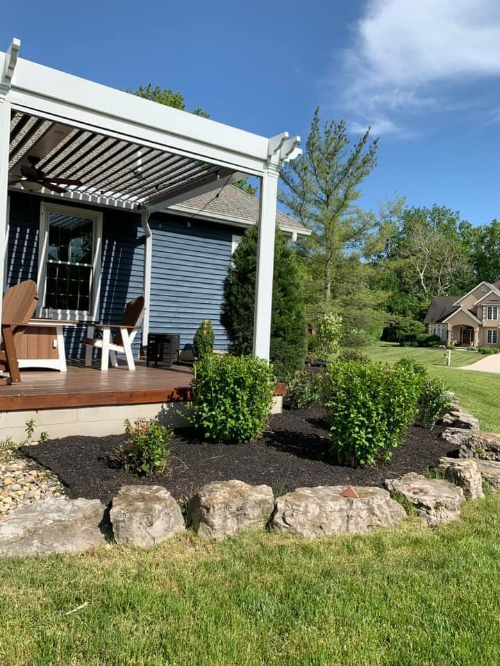 Blue house with white pergola and landscaping, front yard.