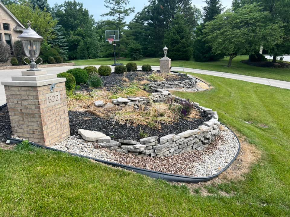 Landscaped yard with stone borders, pillars with lights, address marker, and basketball hoop.
