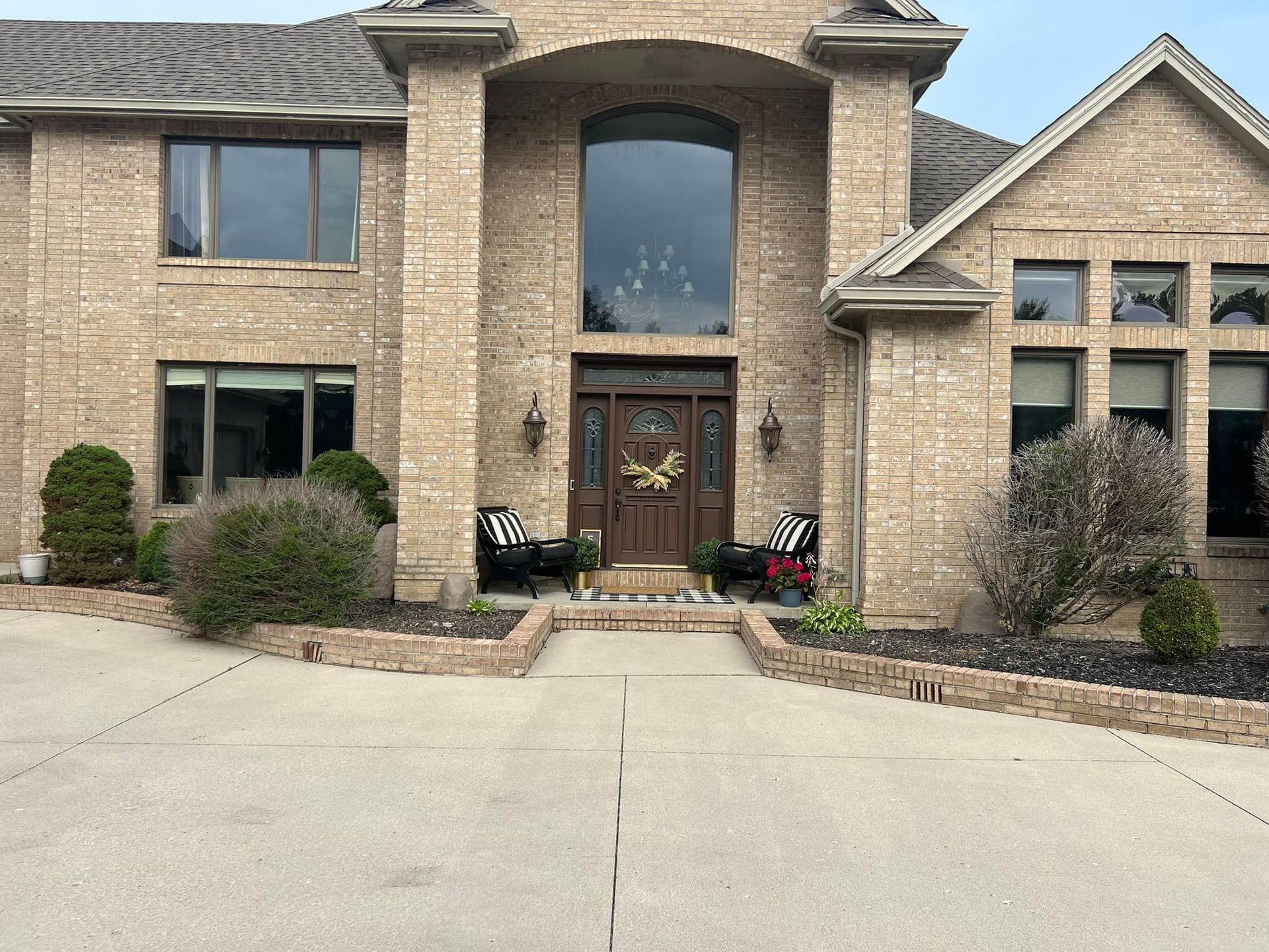 Brick home with a tall arched window above the front door, and two black chairs sit on the porch.