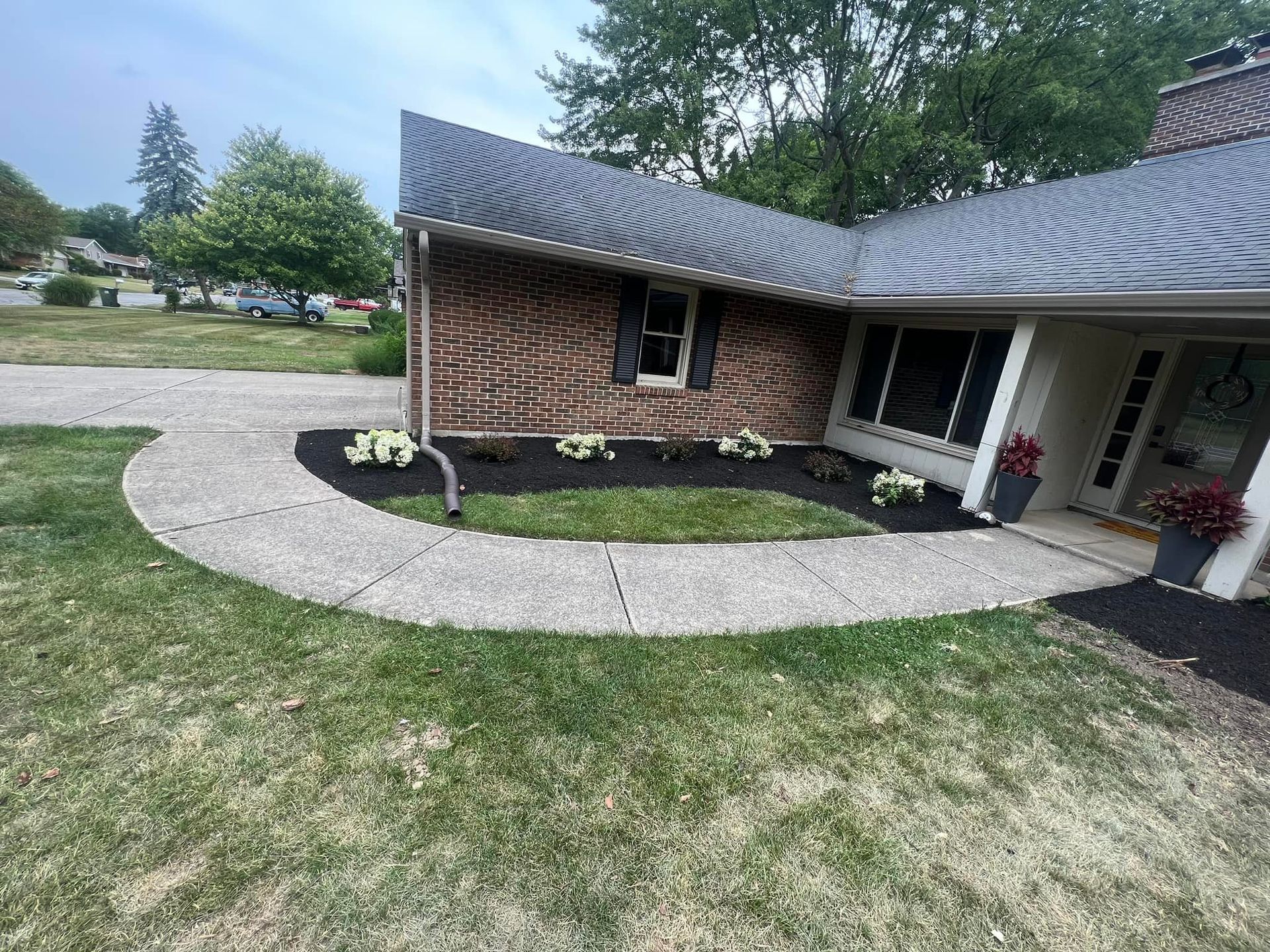 A house with a curved walkway, garden beds with white flowers, and a manicured lawn.