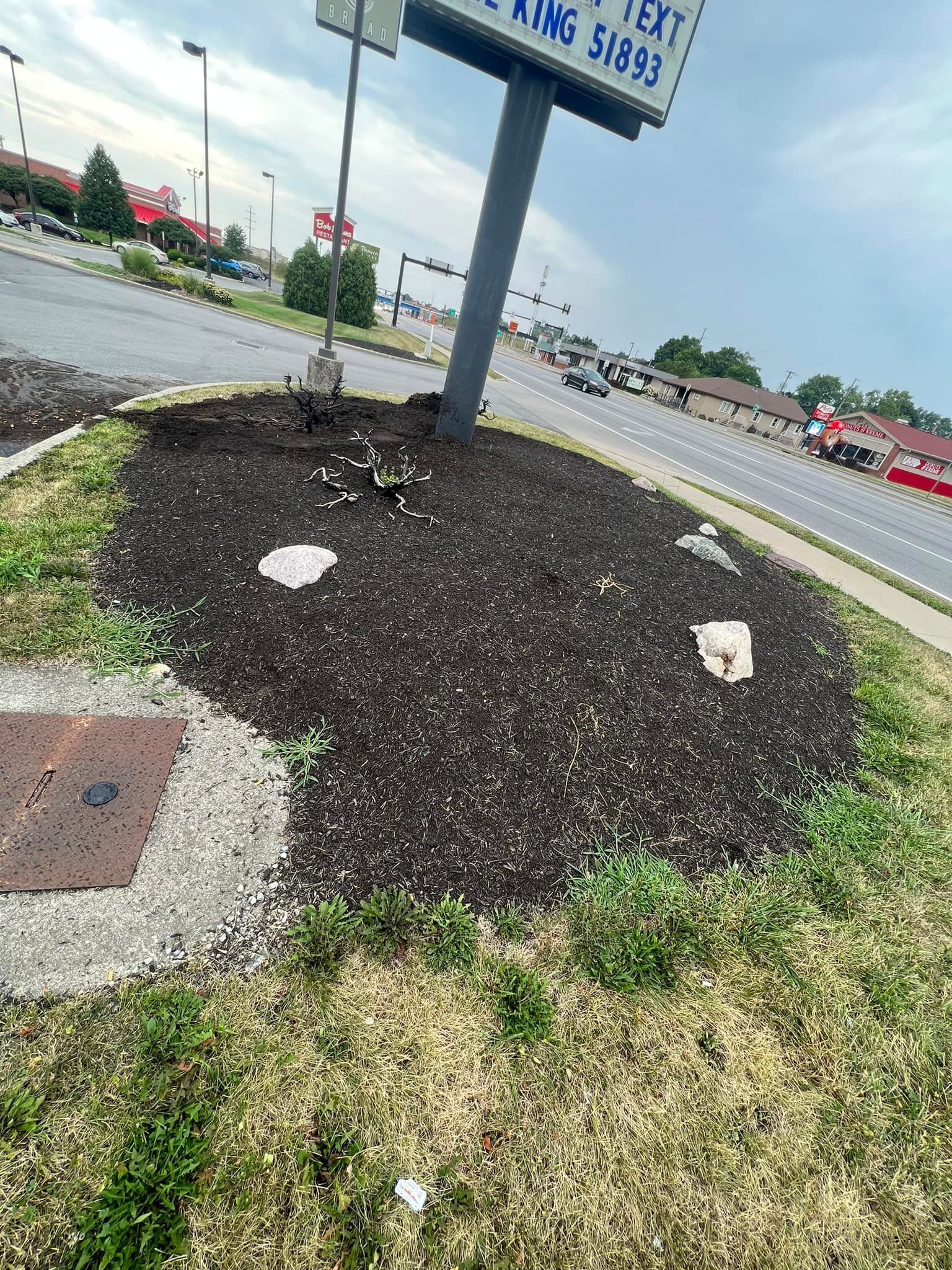 Landscaped area with a sign and dark mulch, beside a road.
