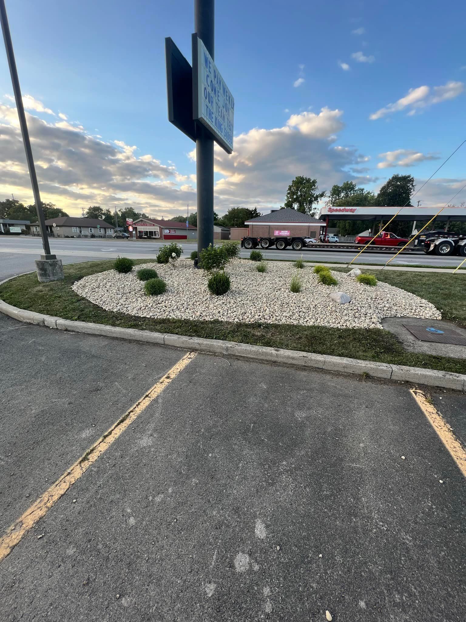 Flowerbed with white rocks, bushes, and sign post in front of a gas station.