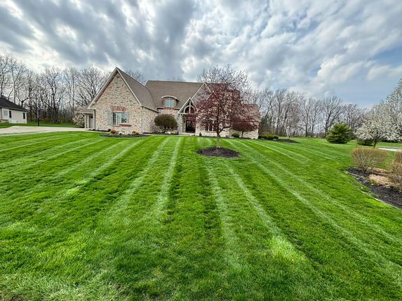 Lush green lawn with striped mowing pattern leading to a large stone house under a cloudy sky.