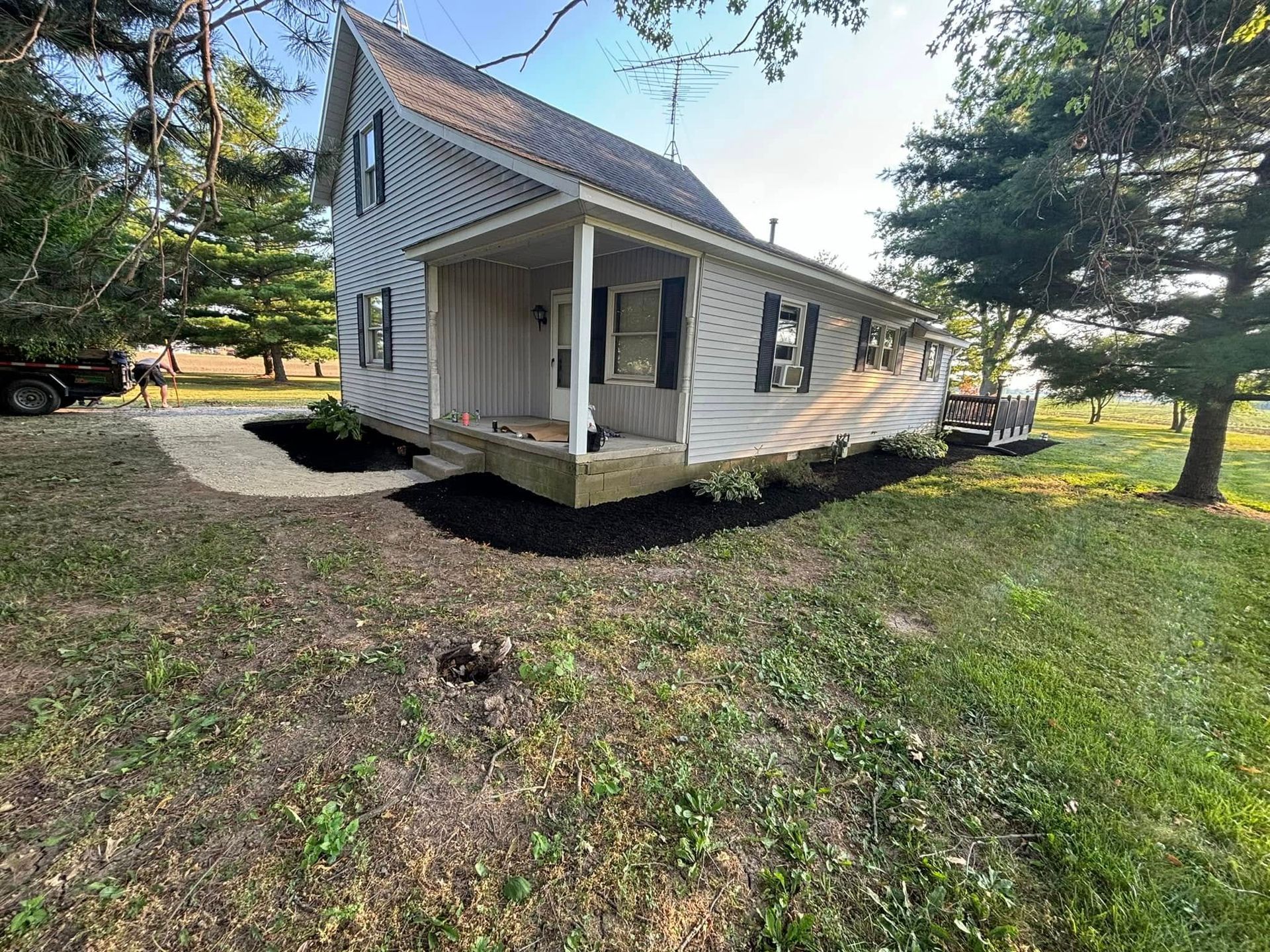 Two-story white house with black shutters and a porch; black mulch and green grass in front yard.