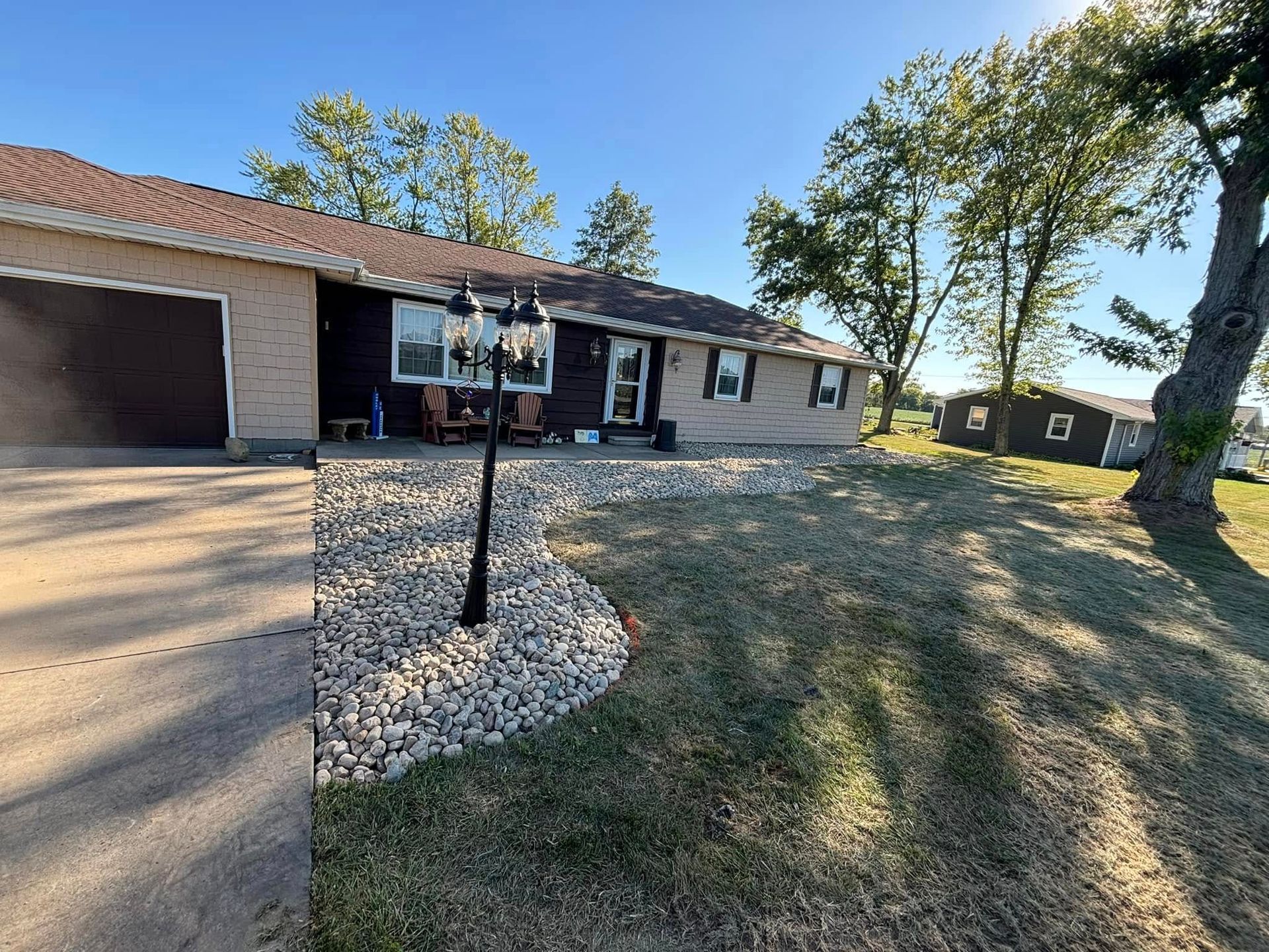 Ranch-style house with stone landscaping, a lamp post, and a driveway. Sunny day.