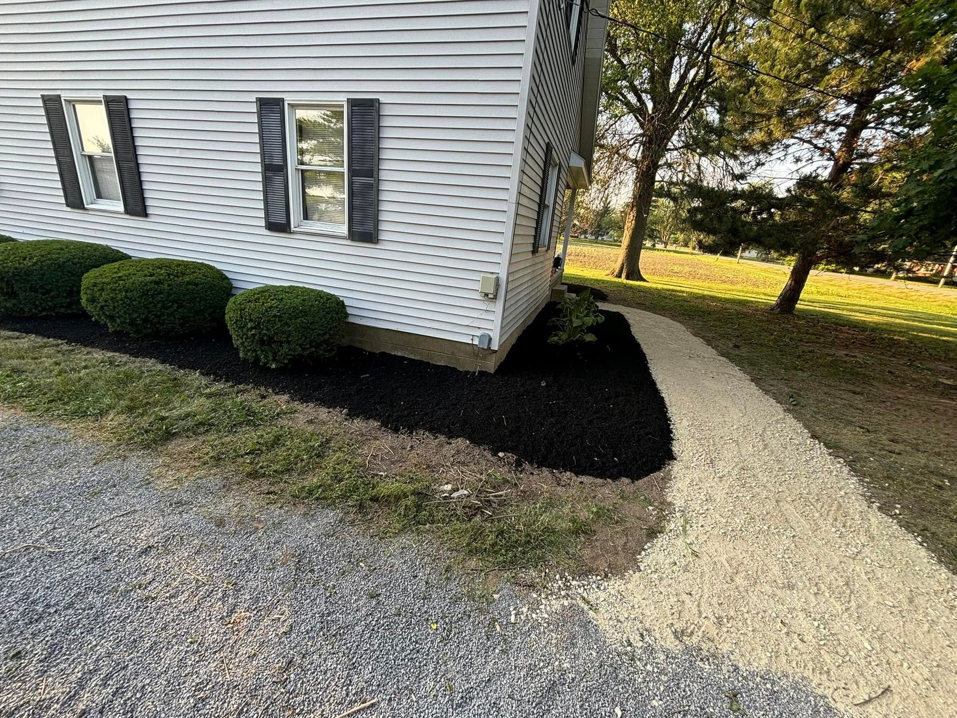 White house with black mulch bed and gravel path.