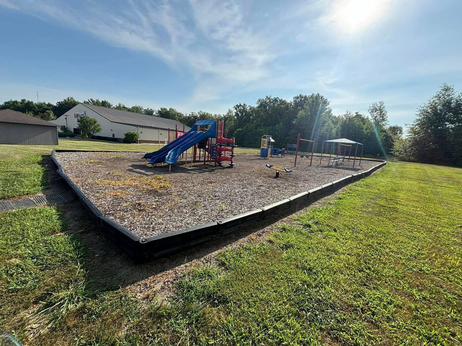 Playground on a sunny day, surrounded by grass, with slides, and other play structures.