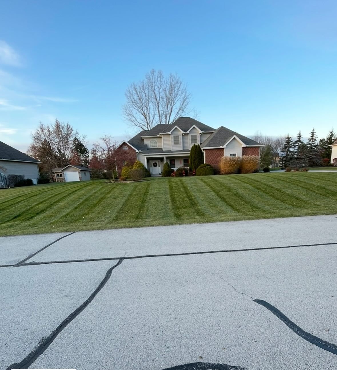 A two-story house with a striped lawn on a sunny day. The street is in the foreground.