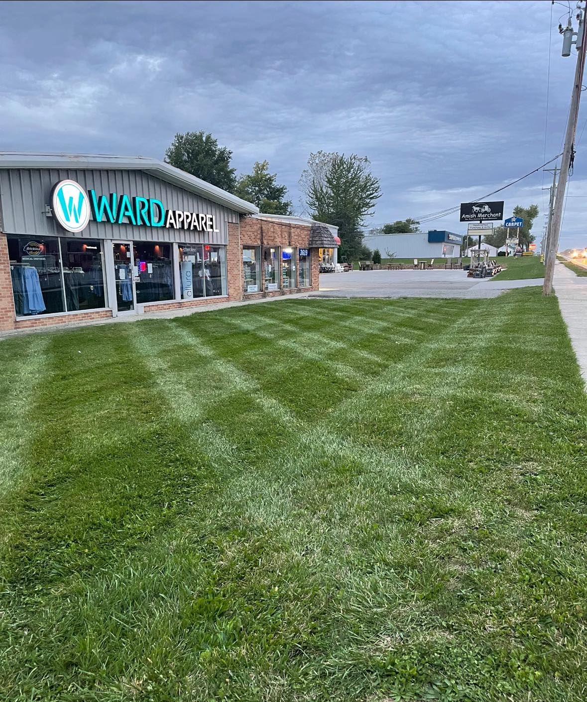 A store, Ward Apparel, with striped freshly mown lawn, under a cloudy sky.