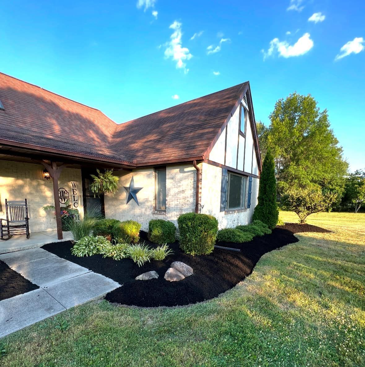 Tudor style home with black mulch beds, green bushes, and a star decoration, under a blue sky.