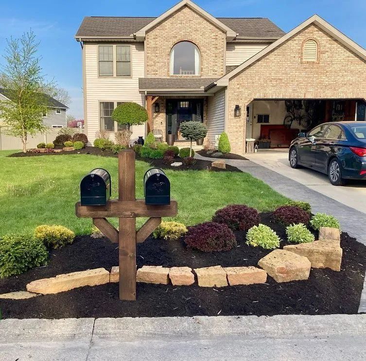 Two black mailboxes on wooden post in front of a house with a landscaped yard and a car in the driveway.