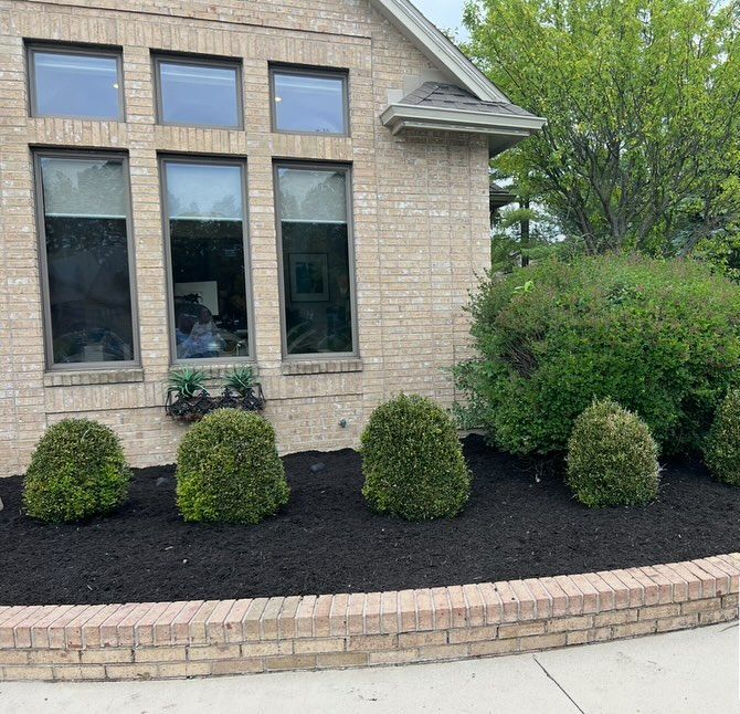 A brick home with dark-tinted windows, a brick-walled garden bed, and trimmed green bushes.
