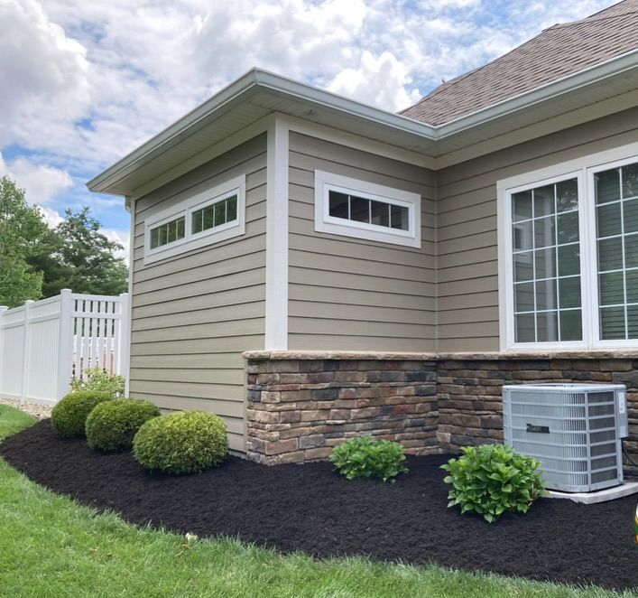 Exterior of a house with tan siding, stone base, and manicured landscaping.