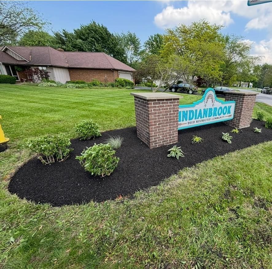 Sign for Indianbrook neighborhood, green grass, brick pillars, black mulch, and landscaped bushes.