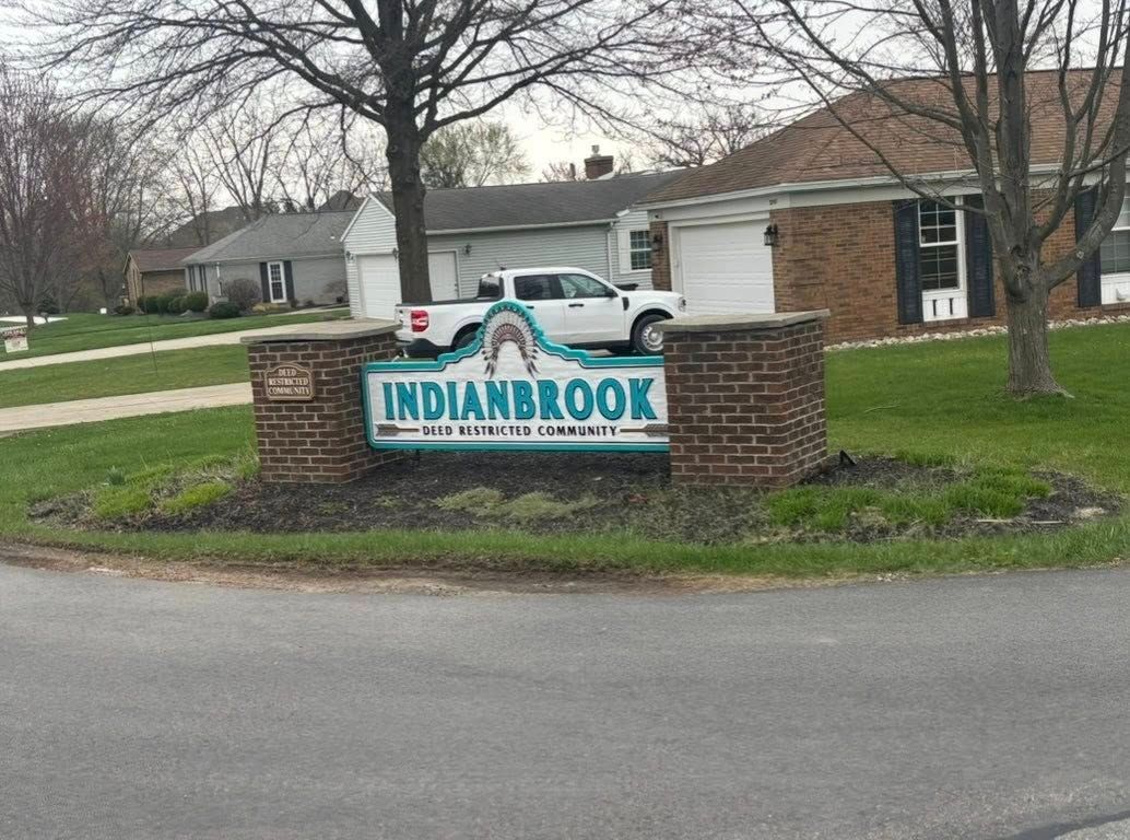 Indianbrook neighborhood sign with a white pickup truck on top, brick pillars, and houses in background.