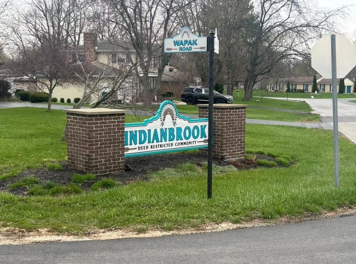 Sign for Indianbrook residential area. Turquoise and white sign on a brick structure, under a street sign.