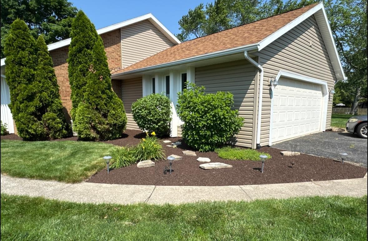 A house with a brown roof, beige siding, and a white garage door, with a well-landscaped yard.