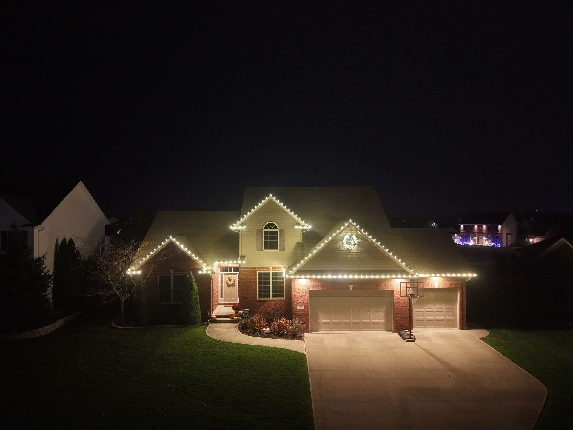 House at night, illuminated with white Christmas lights along rooflines. A moon-shaped decoration is on the roof.