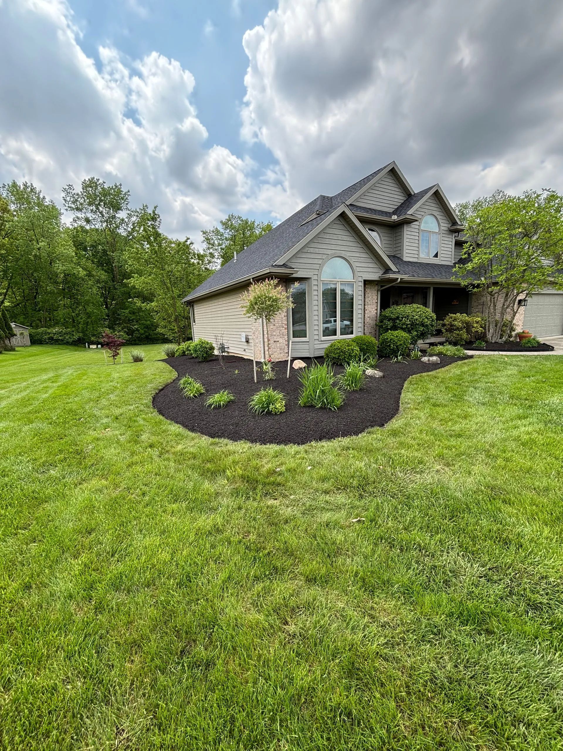Front yard flower bed with pink azaleas beside a house and driveway