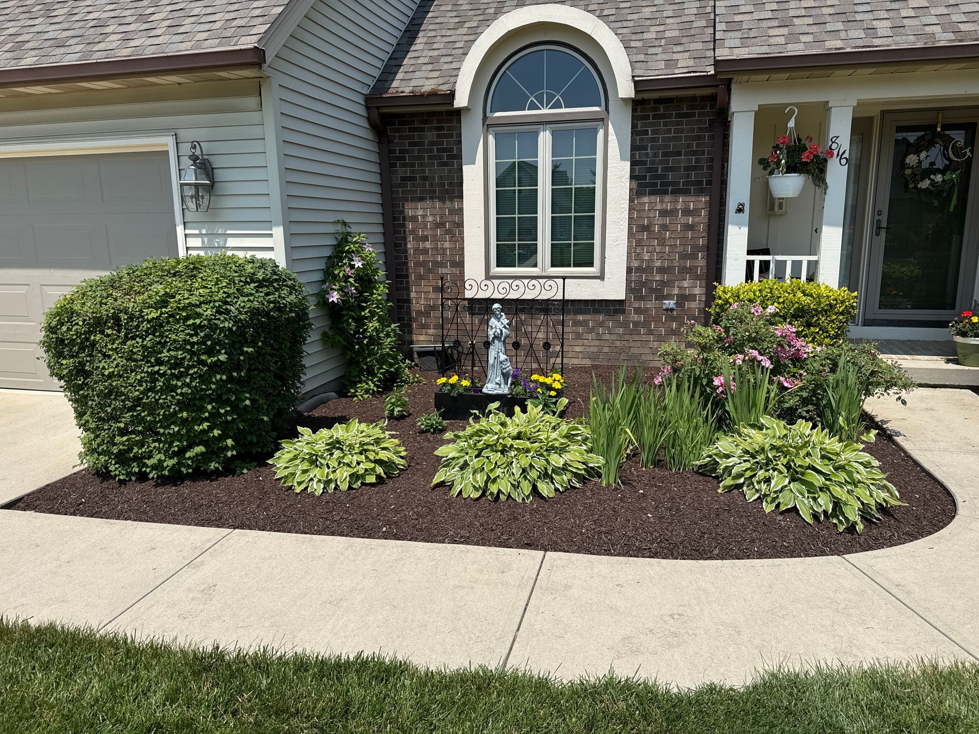 A house with a flower bed featuring green plants and flowers in front of the windows.